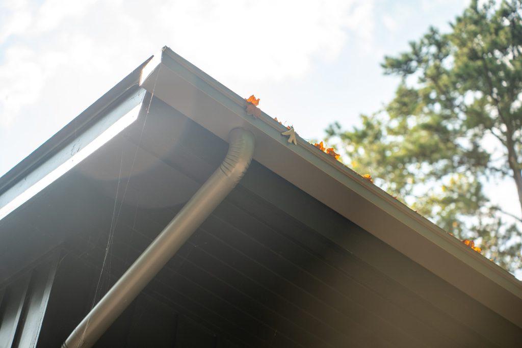 A seamless gutter and downspout under a dark roof edge