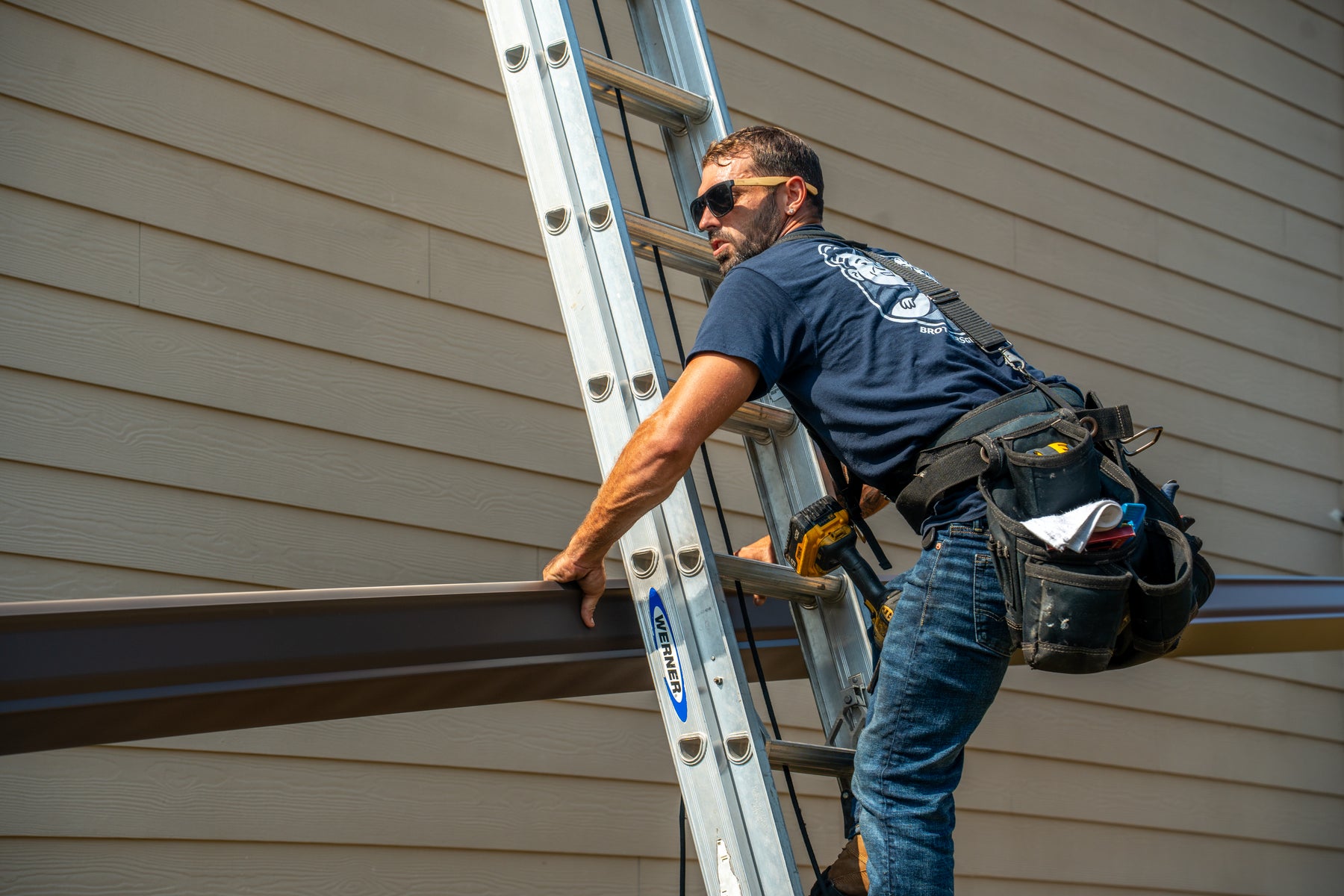 A Brothers that just do Gutters installer carrying a formed gutter run up a ladder