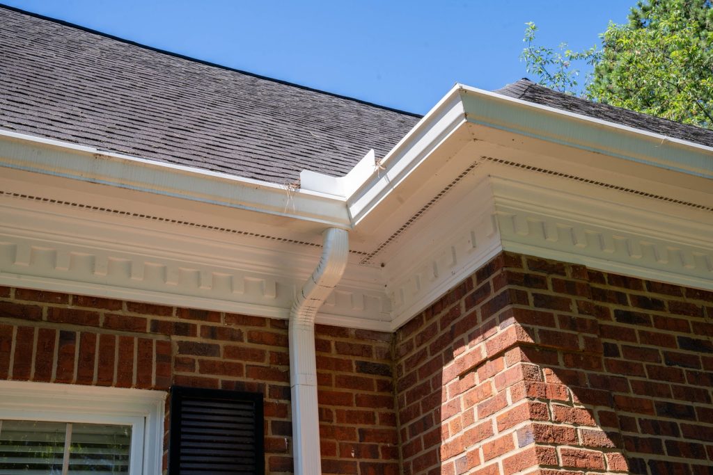 White seamless gutters and a downspout on a brick home